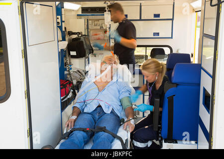 Paramedics treating unconscious elderly man on stretcher in ambulance car Stock Photo