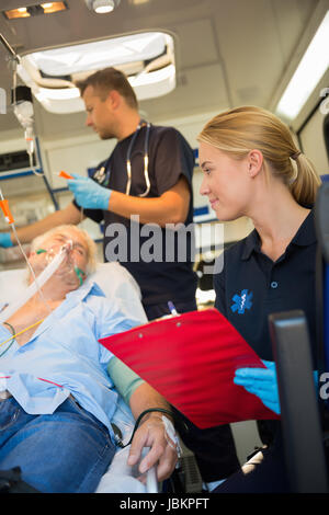 Paramedics examining injured elderly patient on stretcher in ambulance Stock Photo