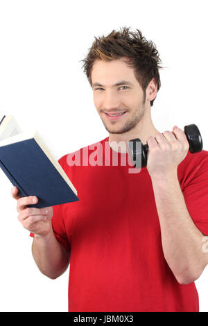 Man reading book whilst lifting weights Stock Photo