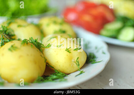 Fresh organic vegetables and boiled new potatoes on the plates on the wooden table. Close up, selective focus. Stock Photo