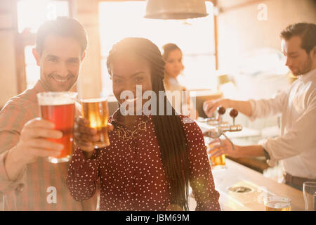Portrait smiling couple toasting beer glasses at bar Stock Photo