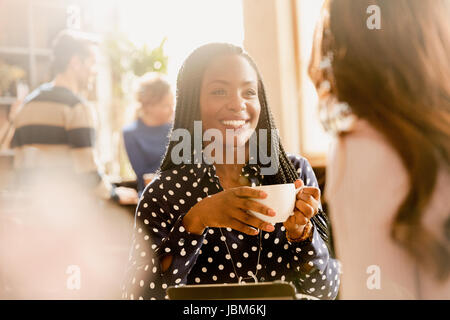 Smiling women friends drinking coffee and talking in cafe Stock Photo