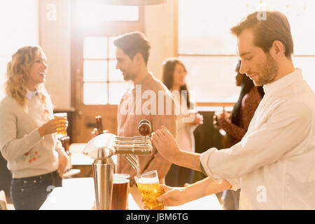 Bartender pouring beer at beer tap behind bar Stock Photo