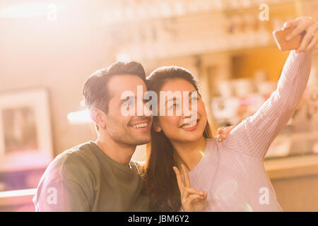 Smiling couple gesturing peace sign taking selfie with camera phone Stock Photo