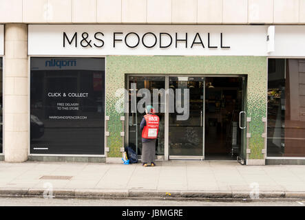 A Big Issue seller outside an M&S Foodhall on Tottenham Court Road, London, England, UK Stock Photo