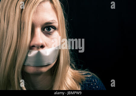 Portrait of scared kidnapped woman hostage with tape over her mouth Stock Photo