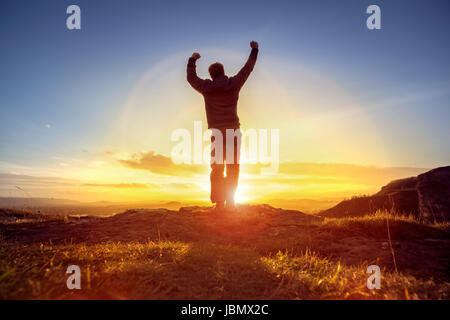 Happy man celebrating winning success or worship and praise against sunset Stock Photo