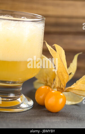 Physalis berries (lat. Physalis peruviana) with a Peruvian cocktail called Aguaymanto Sour (Physalis Sour) prepared from physalis juice, pisco (Peruvian grape hard liquor), syrup and egg white on the side (Selective Focus, Focus on the front of the first physalis berry) Stock Photo