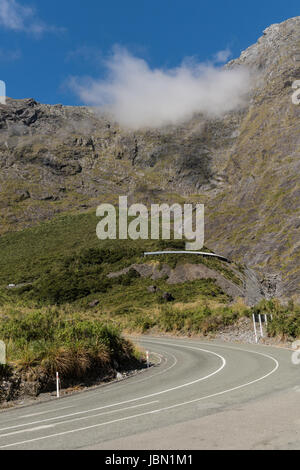 Fiordland National Park, New Zealand - March 16, 2017: Mountain range and road under Hommer Tunnel under blue sky with a faint white cloud band toppin Stock Photo