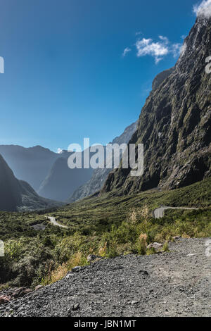 Fiordland National Park, New Zealand - March 16, 2017: Mountain range and road down under Hommer Tunnel under blue sky. Sparse green non-tree vegetati Stock Photo