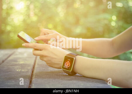 Close up of female hands using smart phone and wearing smart watch with heart rate app displayed at the desk in the park. New technologies and lifesty Stock Photo