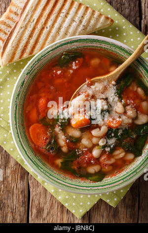 White bean soup with tomatoes, spinach, carrots and parmesan close-up on the table. vertical view from above
