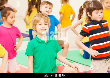 Portrait of happy six years old blond boy bending knee, practicing gymnastics in children's group Stock Photo