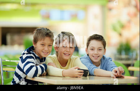 Portrait of three schoolboys sitting at table and looking at camera Stock Photo