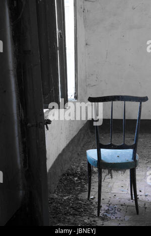 The Blue Cushion-Peeking through the door of this abandoned home, a tattered, blue cushioned chair sits alone in front of a weathered, wood shutter. Stock Photo