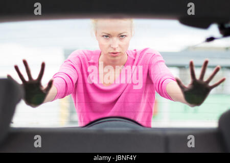 Self-sufficient, strong, young woman pushing a car. Engine breakdown. Stock Photo