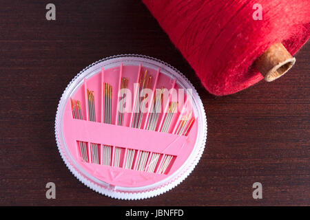 pack of needles and a skein of thread on a wooden background Stock Photo