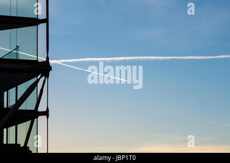 Modern architecture building glass facade constrasting against blue sky with airline jetstreams crossing. Stock Photo