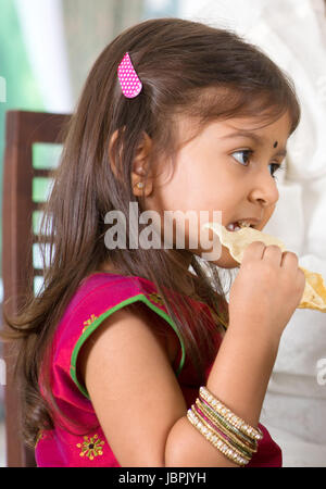 Indian family dining at home. Candid photo of Asian child self feeding snack papadum. India culture. Stock Photo