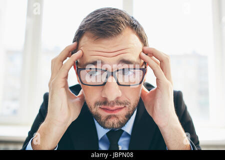 Frustrated businessman in eyeglasses touching his head Stock Photo