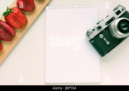 Notebook mock up for artwork with old camera, pen and red strawberries. Top view. Place for text Stock Photo