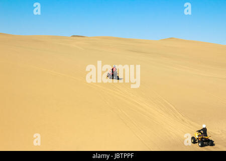 Two happy quad bikers driving in sand dunes. Young active couple in outdoor activity driving quad ATV on coastal desert beach, Africa. Stock Photo