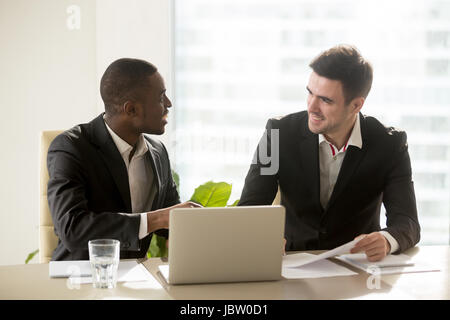 Two accomplished multiracial businessmen discussing idea new business projects at office desk, multi ethnic business group having pleasant funny conve Stock Photo