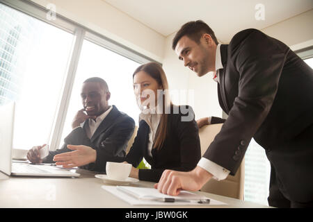 Multiracial business partners using laptop at meeting, looking at screen, busy cheerful executive multi-ethnic team working together in modern office, Stock Photo