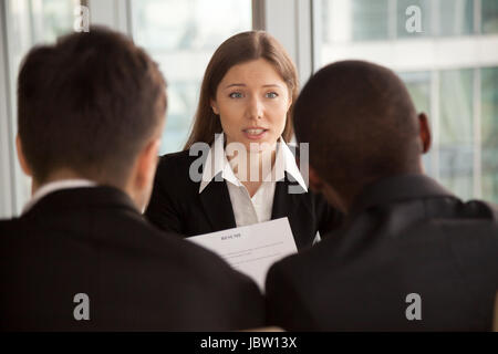 Female applicant introducing herself during job interview, talking about working experience, rear view at multiracial hr management group interviewing Stock Photo