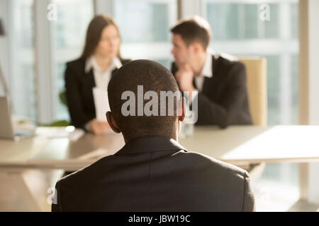 Nervous african-american applicant waiting for result after job interview, hr managers making decision at background, black businessman patiently awai Stock Photo