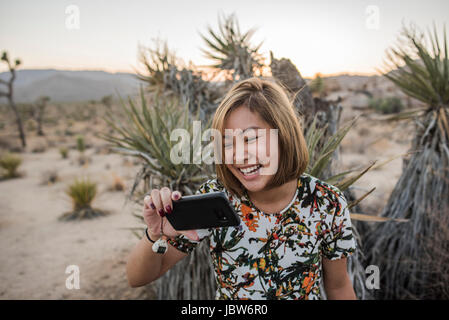 Young woman taking smartphone selfie in Joshua Tree National Park at dusk, California, USA Stock Photo