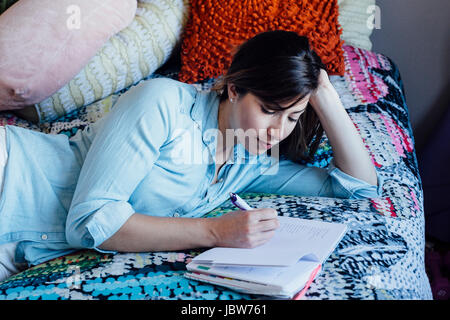Young woman lying on shabby chic bed writing in notebook Stock Photo