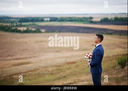 Handsome groom in the middle of the meadow surrounded by tall grass, bushes and rocks. Stock Photo