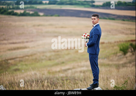 Handsome groom in the middle of the meadow surrounded by tall grass, bushes and rocks. Stock Photo