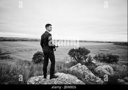 Handsome groom in the middle of the meadow surrounded by tall grass, bushes and rocks. Stock Photo