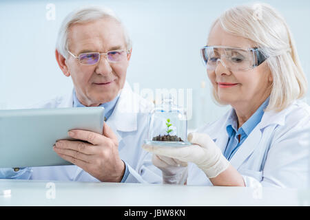 Smiling scientists with digital tablet and green plant in soil Stock Photo