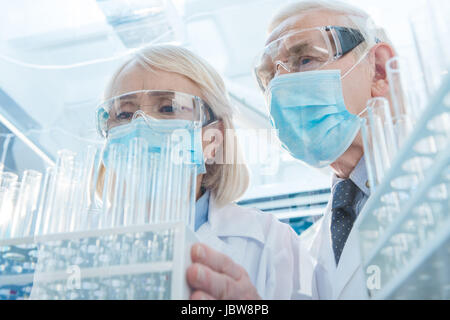 Scientists in protective masks and glasses working with empty test tubes Stock Photo