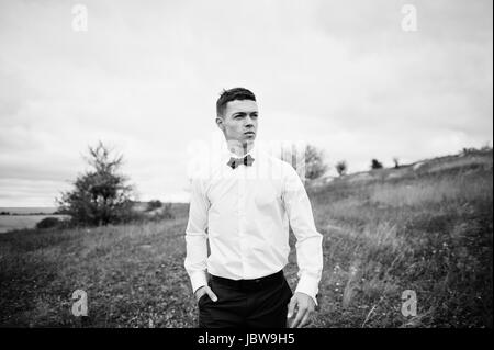 Handsome groom in the middle of the meadow surrounded by tall grass, bushes and rocks. Stock Photo