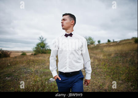 Handsome groom in the middle of the meadow surrounded by tall grass, bushes and rocks. Stock Photo