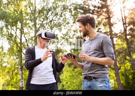 Young man and his senior father with VR glasses outdoors. Stock Photo