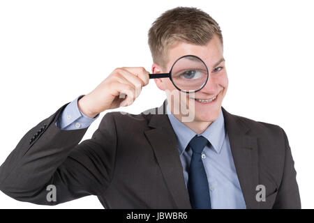 Freigestelltes Foto eines jungen, lächelnden Geschäftsmannes, der durch eine Lupe schaut. Der Mann schaut zur Kamera. Stock Photo