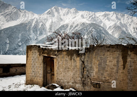 Collapsing building in disrepair with broken stone walls and collapsing door. In the background the majestic Himalaya mountains and snow capped peaks Stock Photo