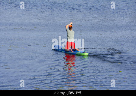 Man on Paddle Board paddling out to lake Stock Photo