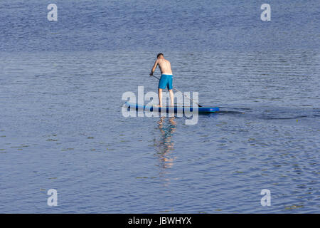 Man on Paddle Board paddling out to lake Stock Photo