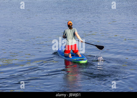 Man on Paddle Board paddling out to lake Stock Photo