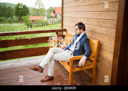 Businessman with smart phone sitting on front porch. Stock Photo