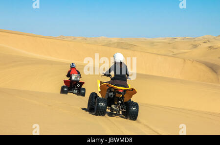 Two happy quad bikers driving in sand dunes. Young active couple in outdoor activity driving quad ATV on coastal desert beach, Africa. Stock Photo