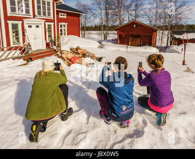 Tourists having fun taking pictures of locals sunbathing. Kangos is a locality situated in Pajala Municipality, Norrbotten County, Swedish Lapland. Stock Photo