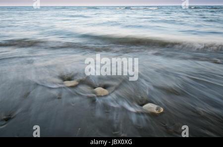 Pebbles on  the beach on a black sand and flowing sea water creating nice textures. Long exposure image. Stock Photo