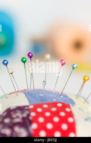 closeup sewing tools, patchwork, tailoring and fashion concept - macro with colorful stitched pincushion and many beautiful pins, background skeins of pink and blue thread, selective focus, vertical. Stock Photo